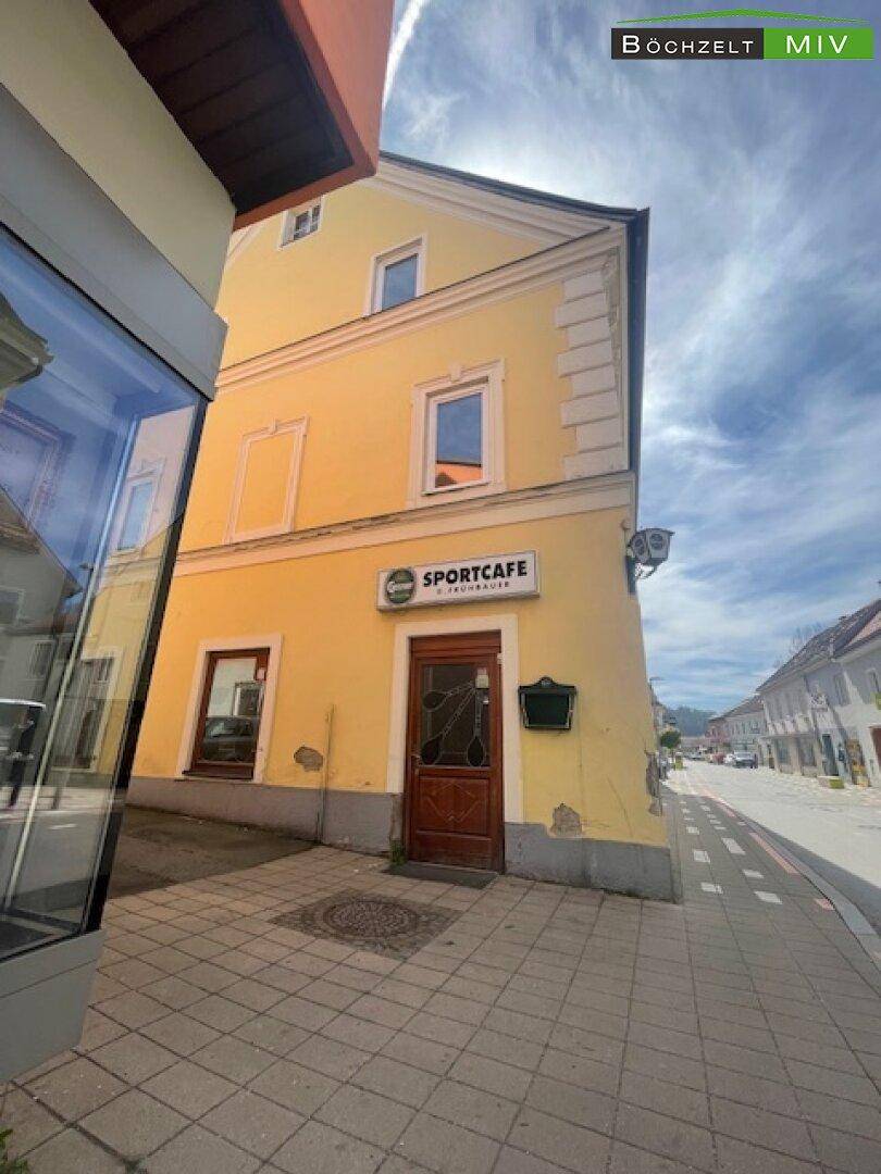 Gelbes Eckgebäude mit Sportcafé im Erdgeschoss, aufgenommen aus einer anderen Perspektive mit blauem Himmel.