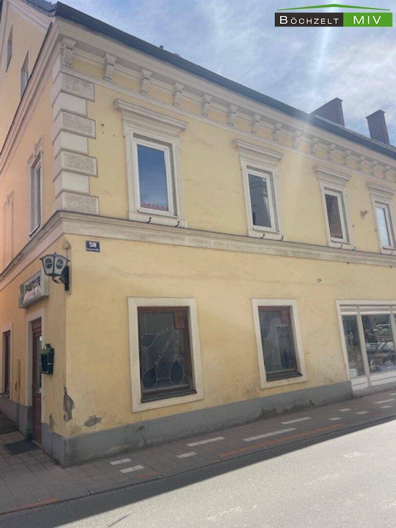 Historisches gelbes Gebäude mit mehreren Fenstern und einem Geschäft im Erdgeschoss an einer belebten Straße.