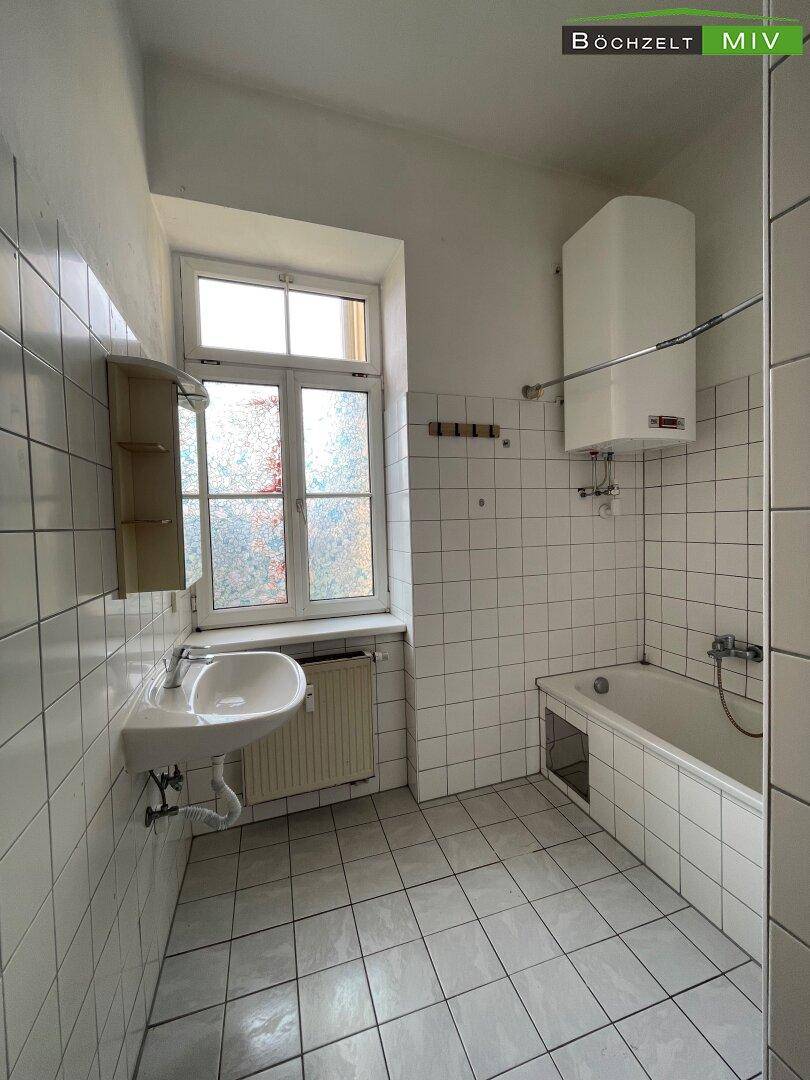 Helles Badezimmer mit Fenster, Waschbecken, Badewanne und weißer Fliesenverkleidung.