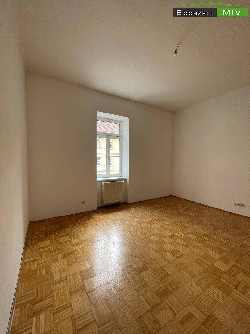 Geräumiges, leeres Zimmer mit klassischem Parkettboden und einem Fenster für natürliche Belichtung.