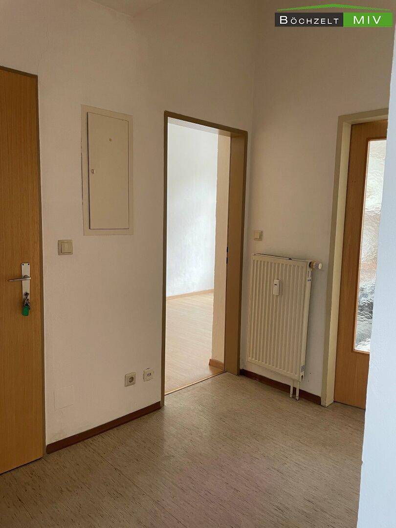 Heller Flur mit Linoleumboden, Holztüren und einem Heizkörper, der zu weiteren Räumen führt.