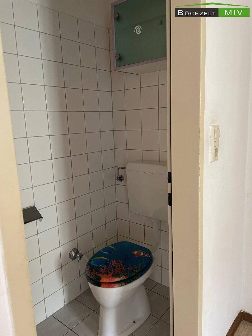 Kleines, gefliestes WC mit Toilette und einem farbenfrohen Toilettensitz.
