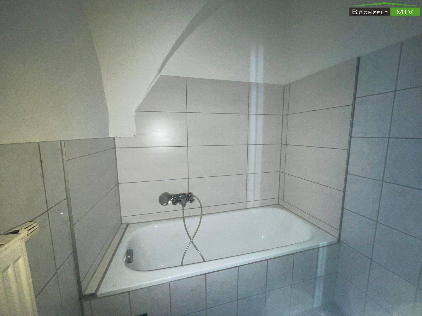 Badezimmer mit Badewanne und weißen Fliesen, unter einer schrägen Decke im Dachgeschossbereich.