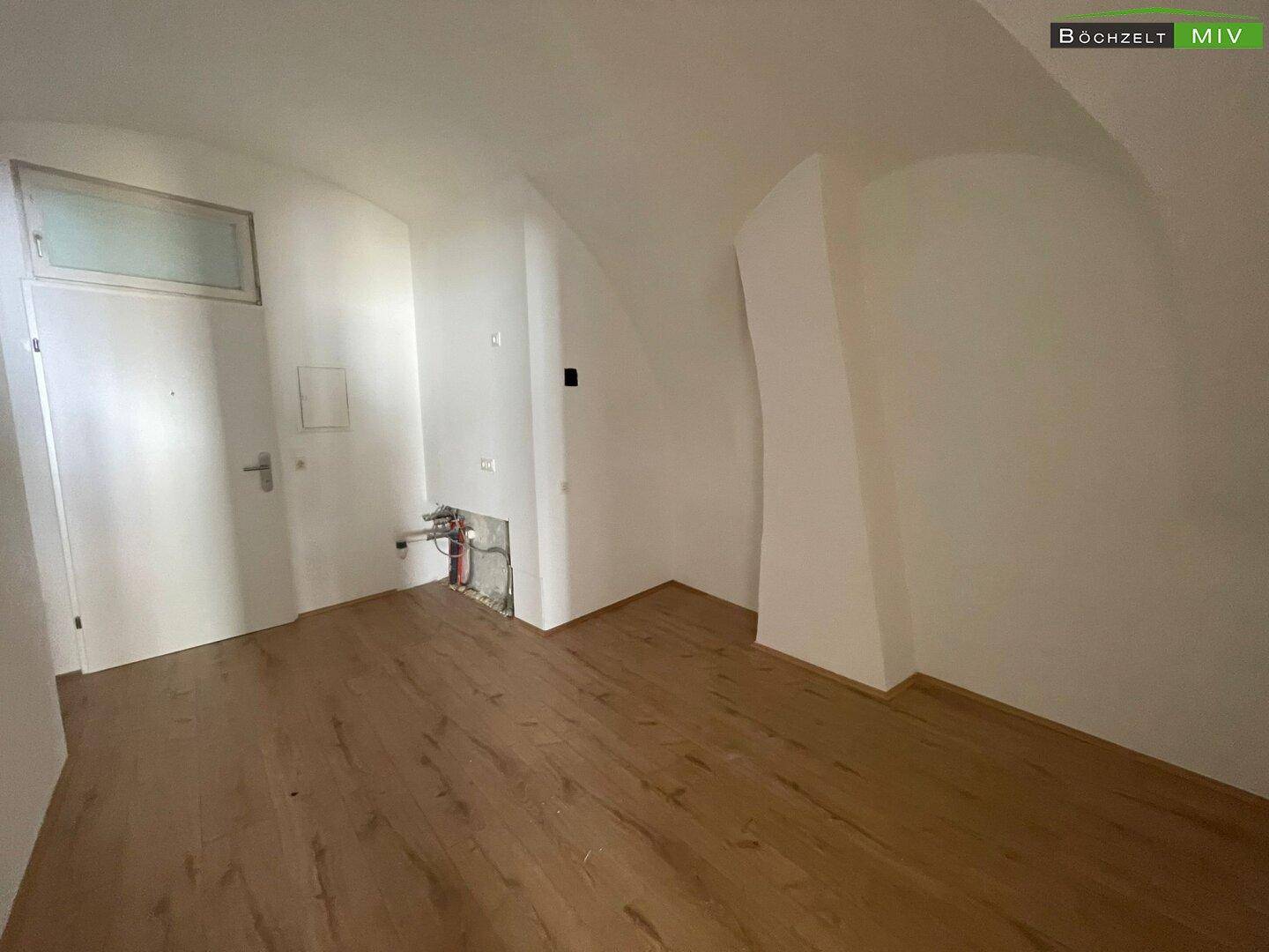 Bereich mit Holzboden und sichtbaren Installationen, vorbereitet für die Küchenmontage oder einen Hauswirtschaftsraum.
