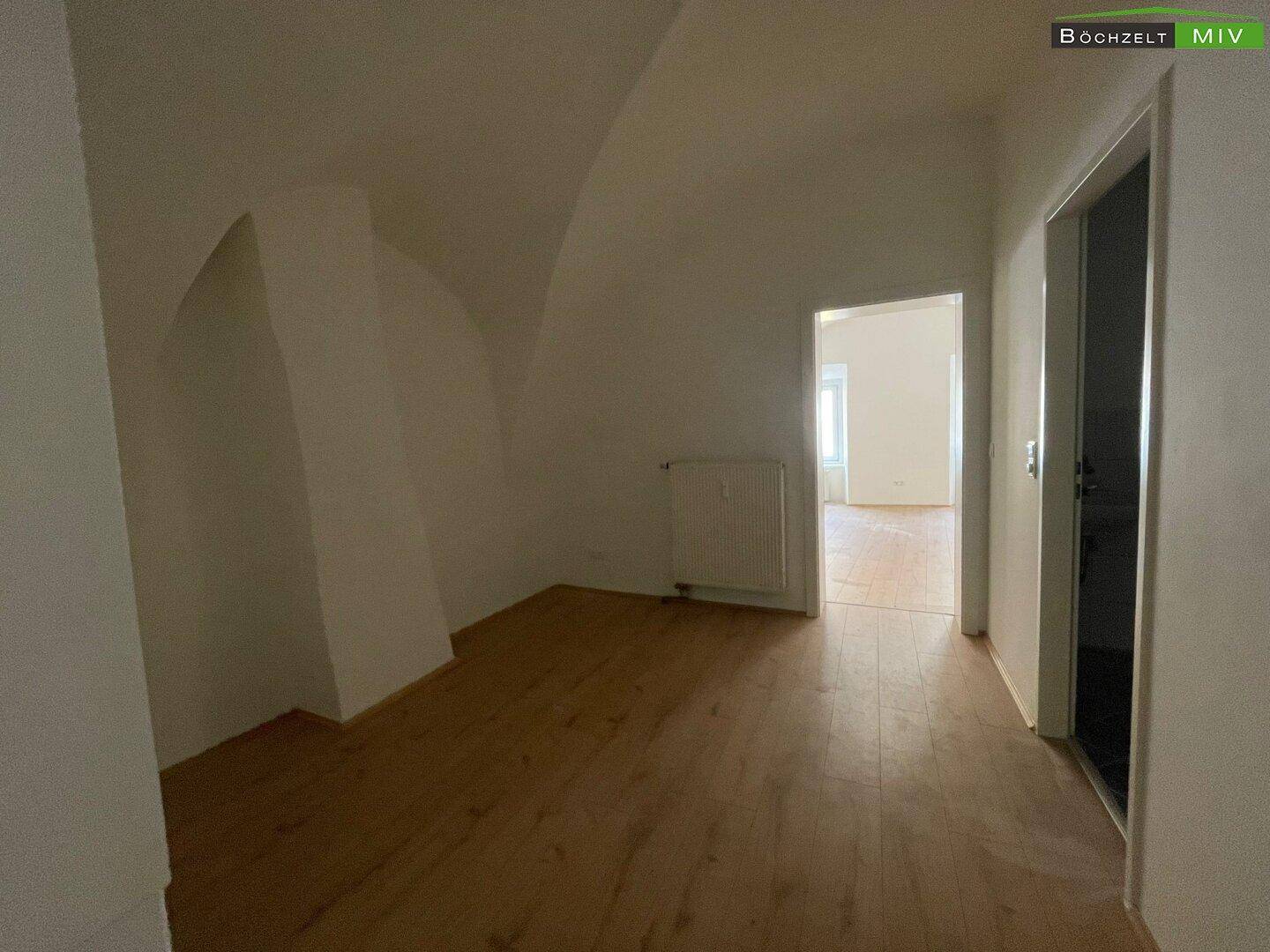 Flur mit Holzboden und Zugang zu weiteren hellen Räumen, unter einer eleganten gewölbten Decke.