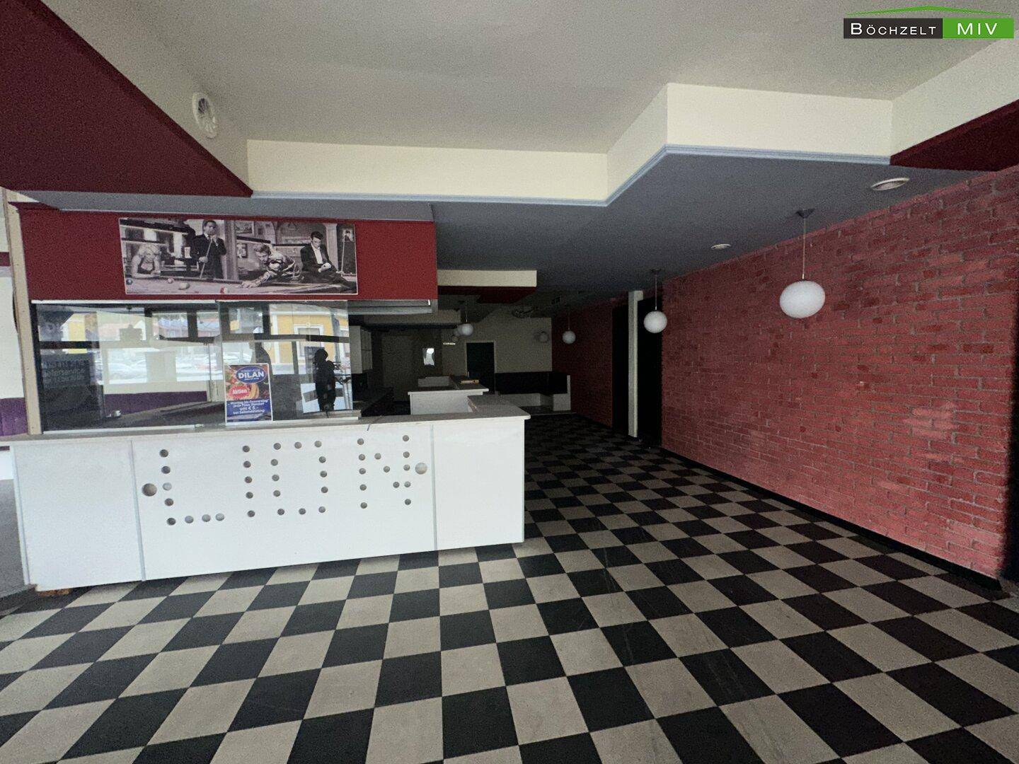 Geräumiger Barbereich mit Schachbrettboden, roter Ziegelwand und Theke in einem Nachtclub.