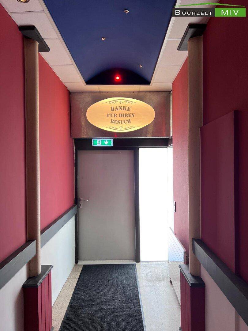 Enger Flur mit roten Wänden, blauer Decke und Säulen, der zu einem Ausgang führt.