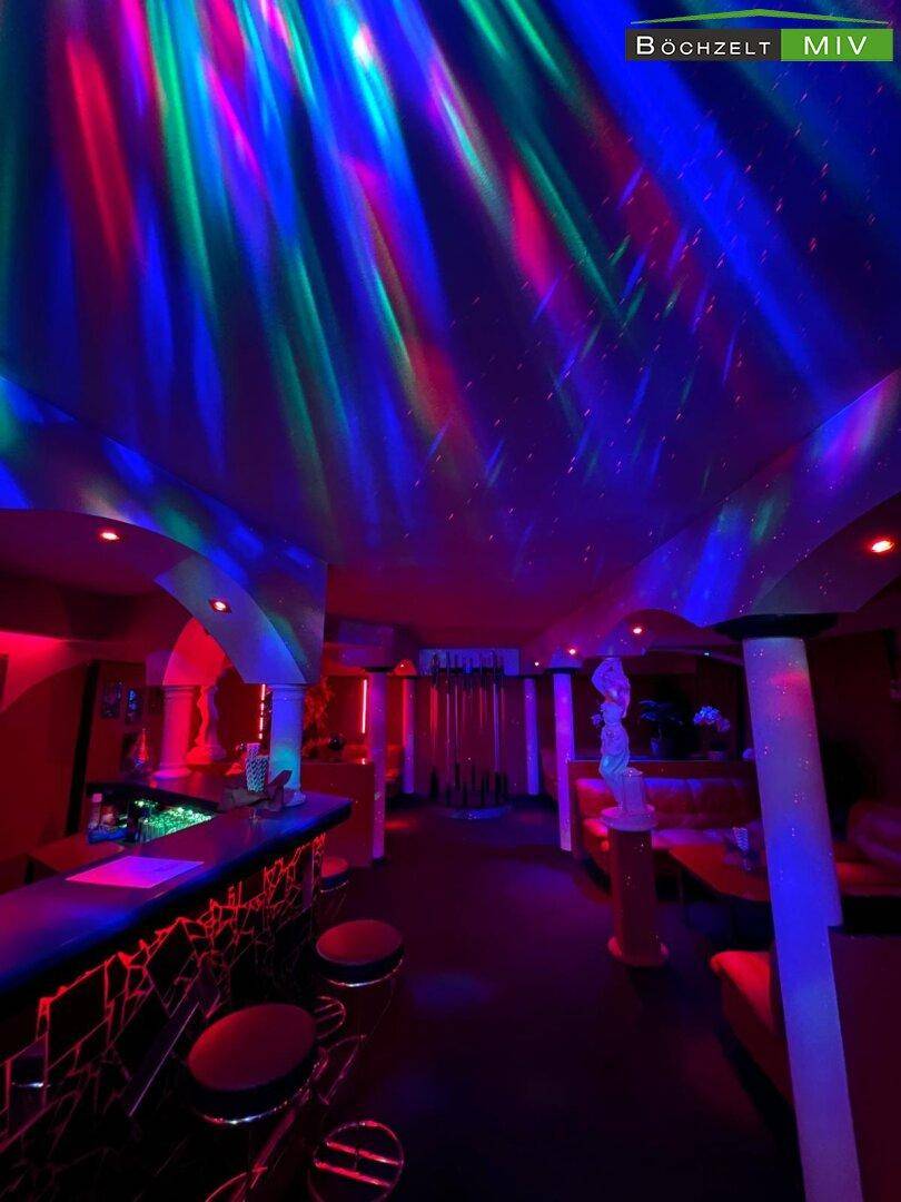 Nachtclub-Interieur mit farbiger Laserbeleuchtung, Bar und Sitzbereichen in lebhaften Rottönen.