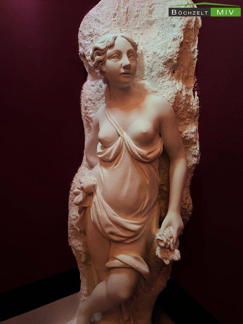 Detailaufnahme einer klassischen weißen Statue vor einem dunklen, roten Hintergrund.