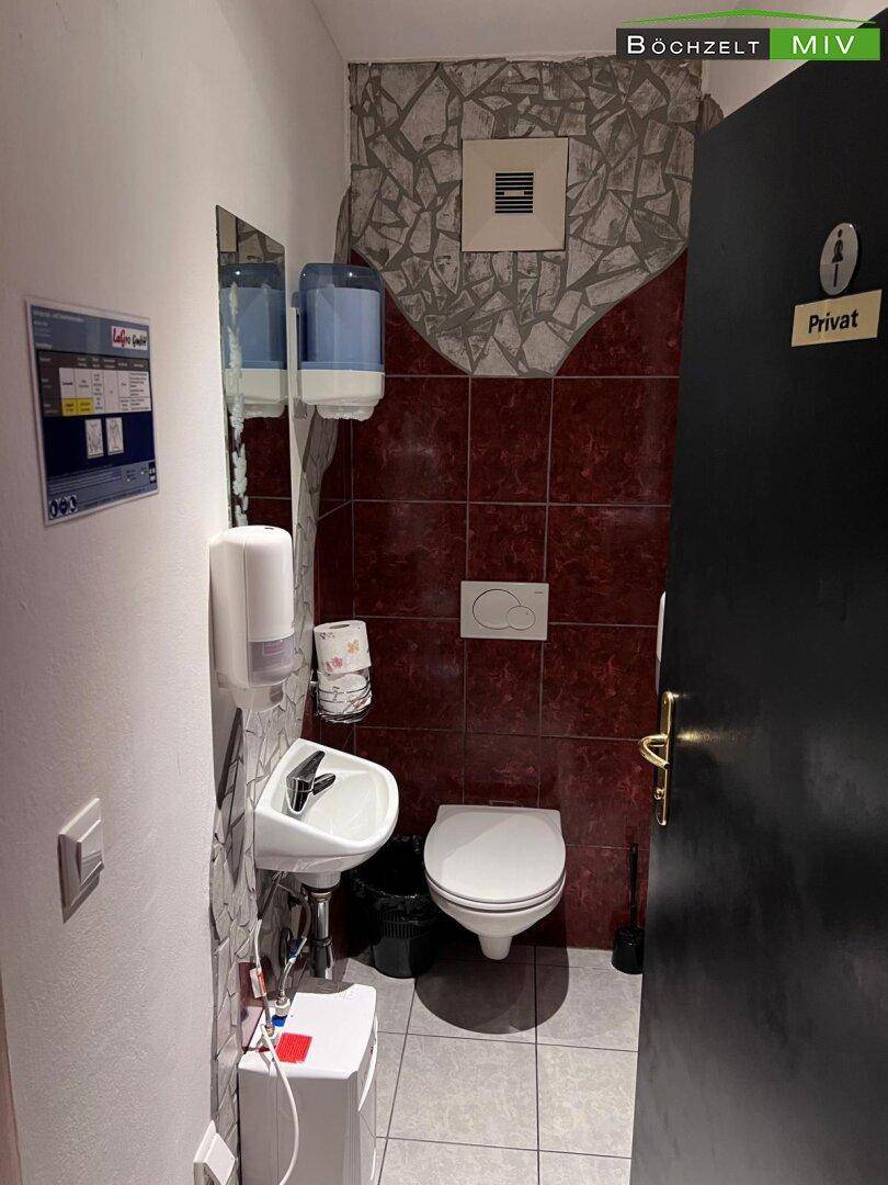 Kleine Gästetoilette mit Waschbecken, WC und Fliesen in Rot- und Grautönen.