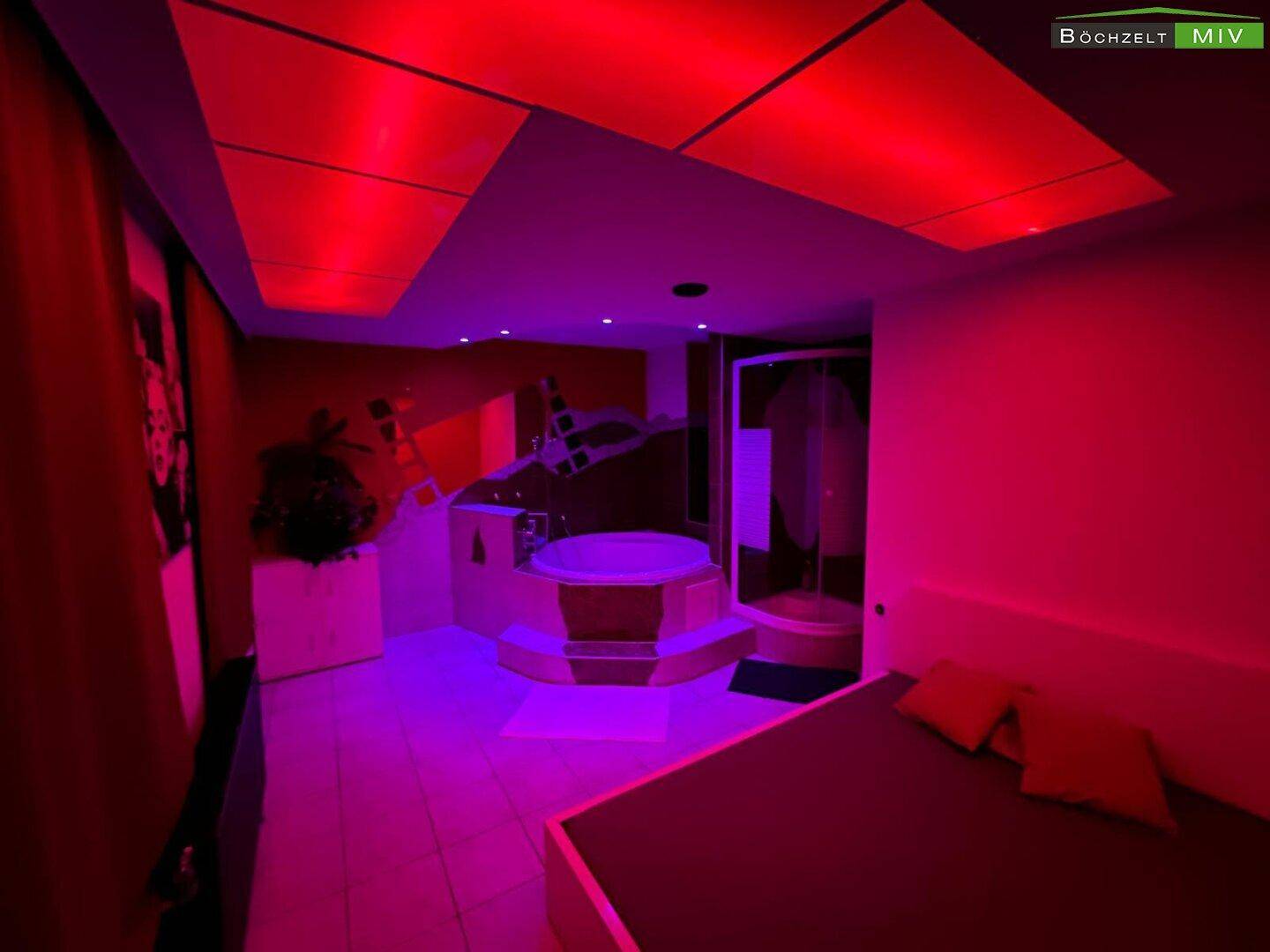 Thematisches Schlafzimmer mit Whirlpool, Dusche und roter Beleuchtung für eine besondere Atmosphäre.