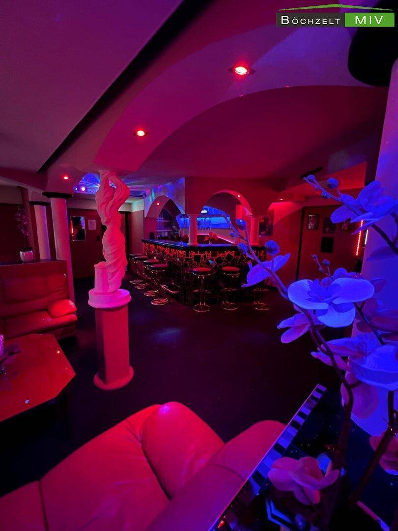 Lounge-Bereich eines Nachtclubs mit roter Beleuchtung, Statuen und bequemen Sitzgelegenheiten.