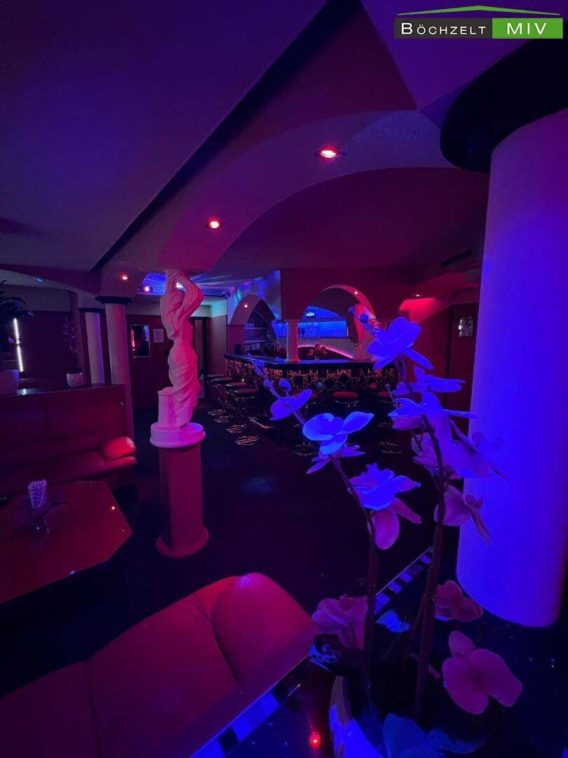 Lounge-Bereich eines Nachtclubs mit roter und blauer Beleuchtung, Statuen und bequemen Sitzgelegenheiten.
