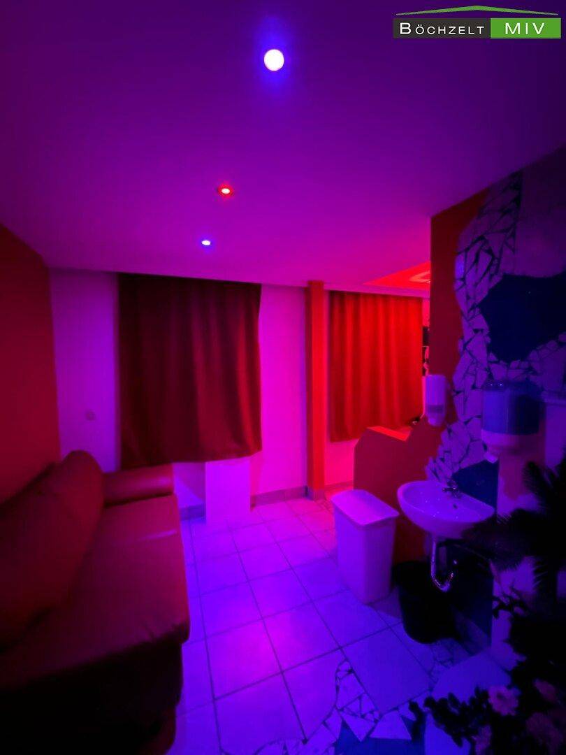 Lounge-Bereich mit Sitzgelegenheiten, Waschbecken und farbiger Beleuchtung in Rot und Lila.
