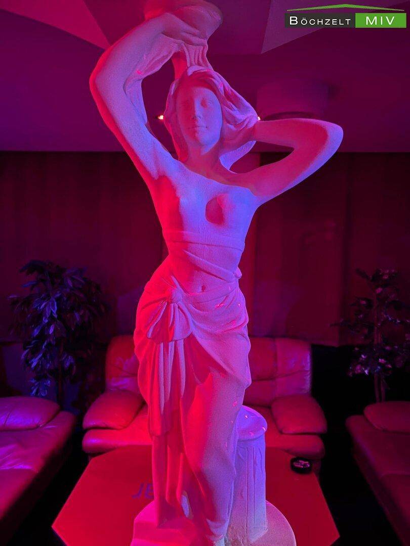 Große weiße Statue einer weiblichen Figur, beleuchtet in Rot und Lila, als Dekoration.