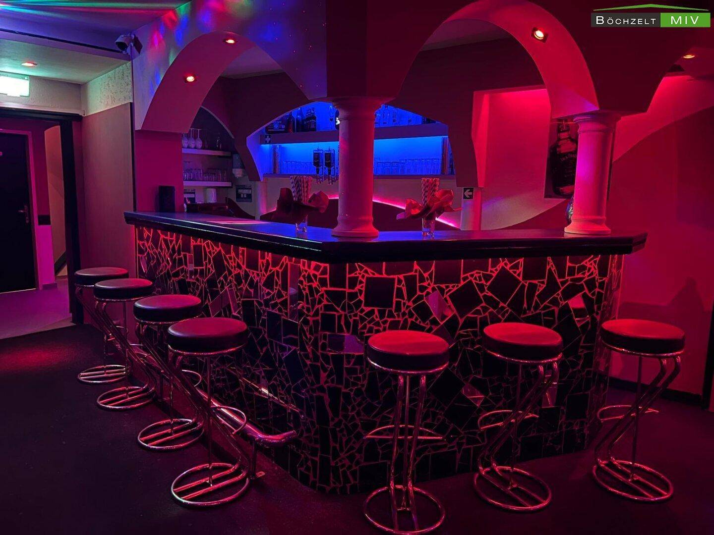 Hauptbarbereich eines Nachtclubs mit beleuchteter Theke, Barhockern und Bögen in Rot.