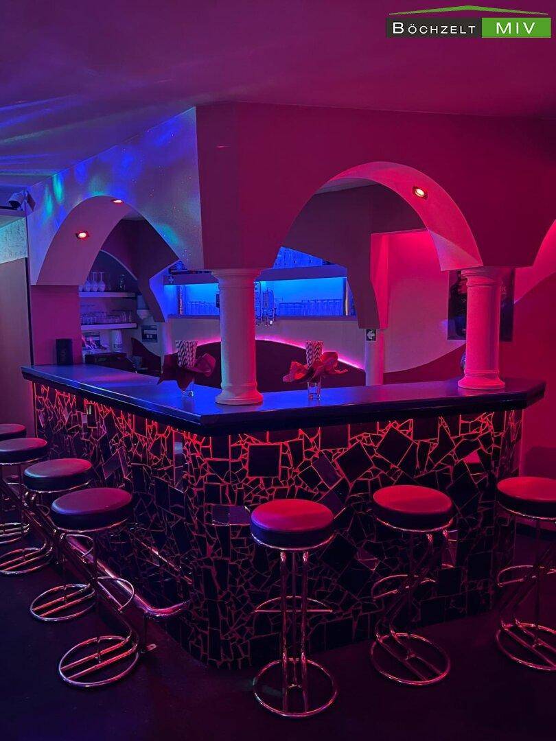 Hauptbarbereich eines Nachtclubs mit beleuchteter Theke, Barhockern und Bögen in Rot.