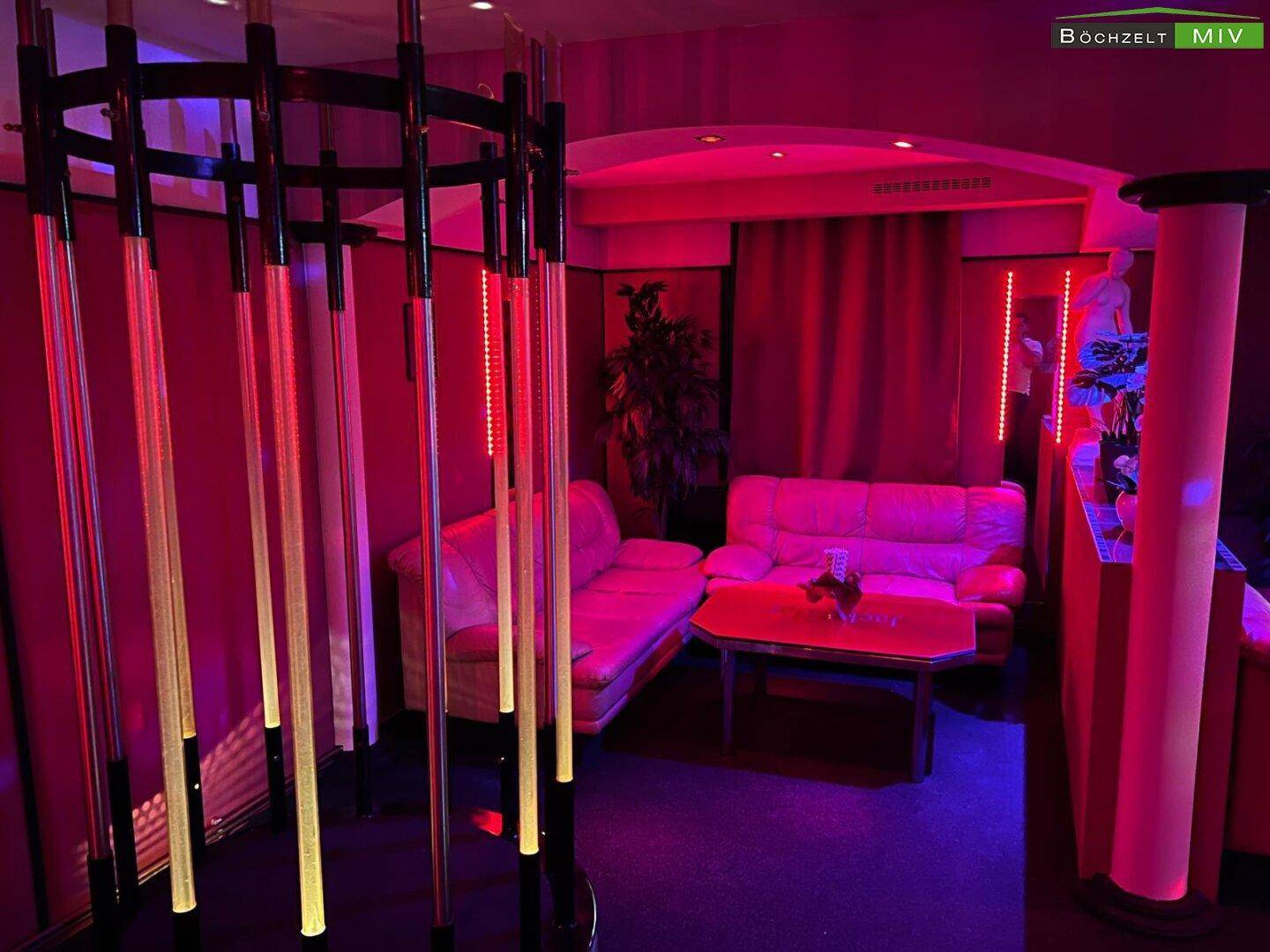 Lounge-Bereich mit roten Sofas, Tischen und dekorativen Säulen, beleuchtet in Rot und Blau.