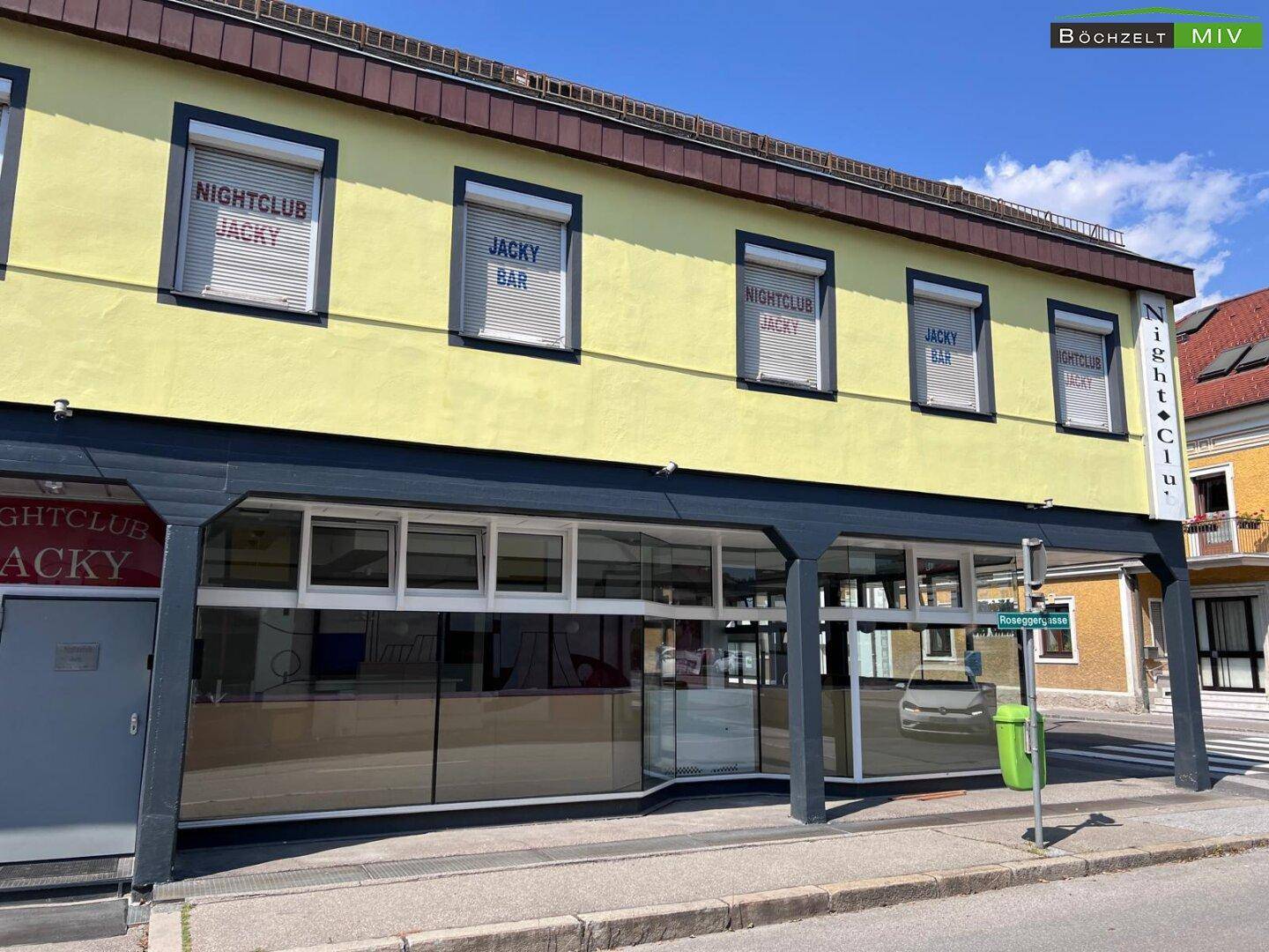 Frontansicht des Gebäudes mit gelber Fassade, großen Fenstern und Beschriftungen für Nachtclub und Bar.