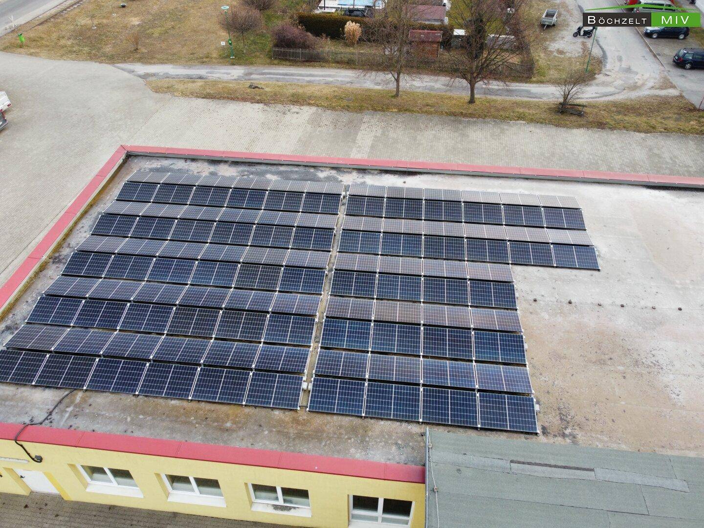 Nahaufnahme der Photovoltaikanlage auf dem Flachdach eines gelben Gebäudes, umgeben von einer weiten Fläche.