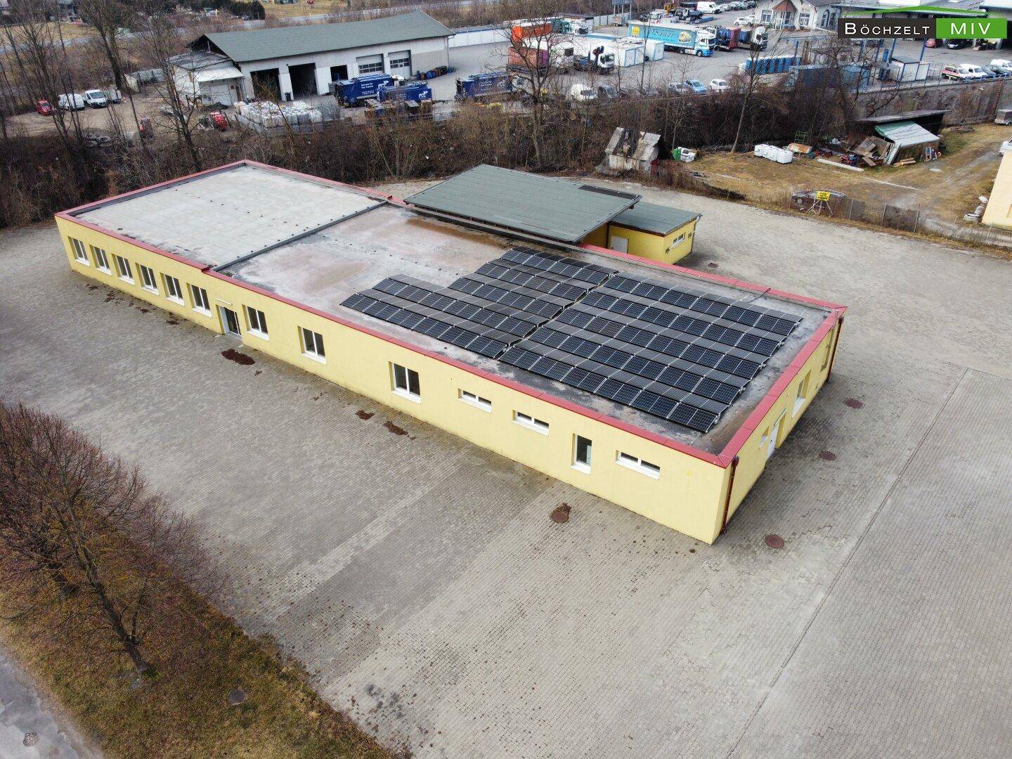 Gelbes Gebäude mit Solaranlage auf dem Dach und einem überdachten Bereich, umgeben von einem weitläufigen Gelände.