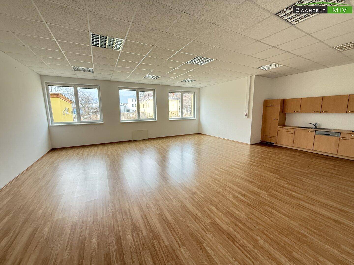Großer, heller Raum mit Laminatboden und einer einfachen Küchenzeile entlang einer Wand.