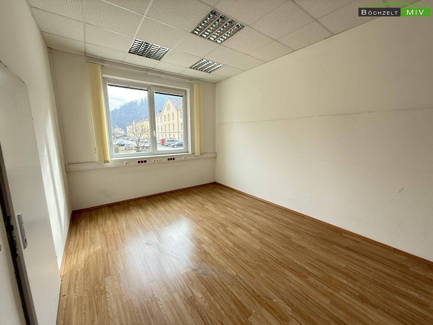 Leeres Büro mit Laminatboden und einem großen Fenster, das einen Blick auf die Umgebung bietet.