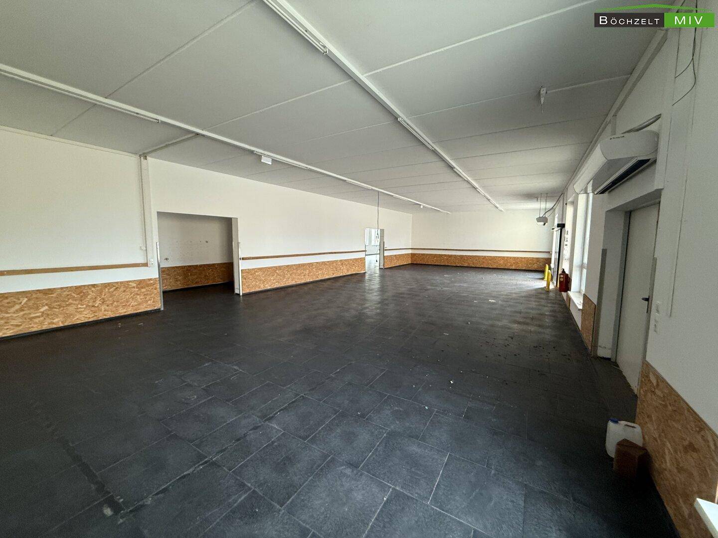 Geräumiger, offener Bereich mit dunklem Fliesenboden und teilweise verkleideten Wänden, geeignet für verschiedene Zwecke.