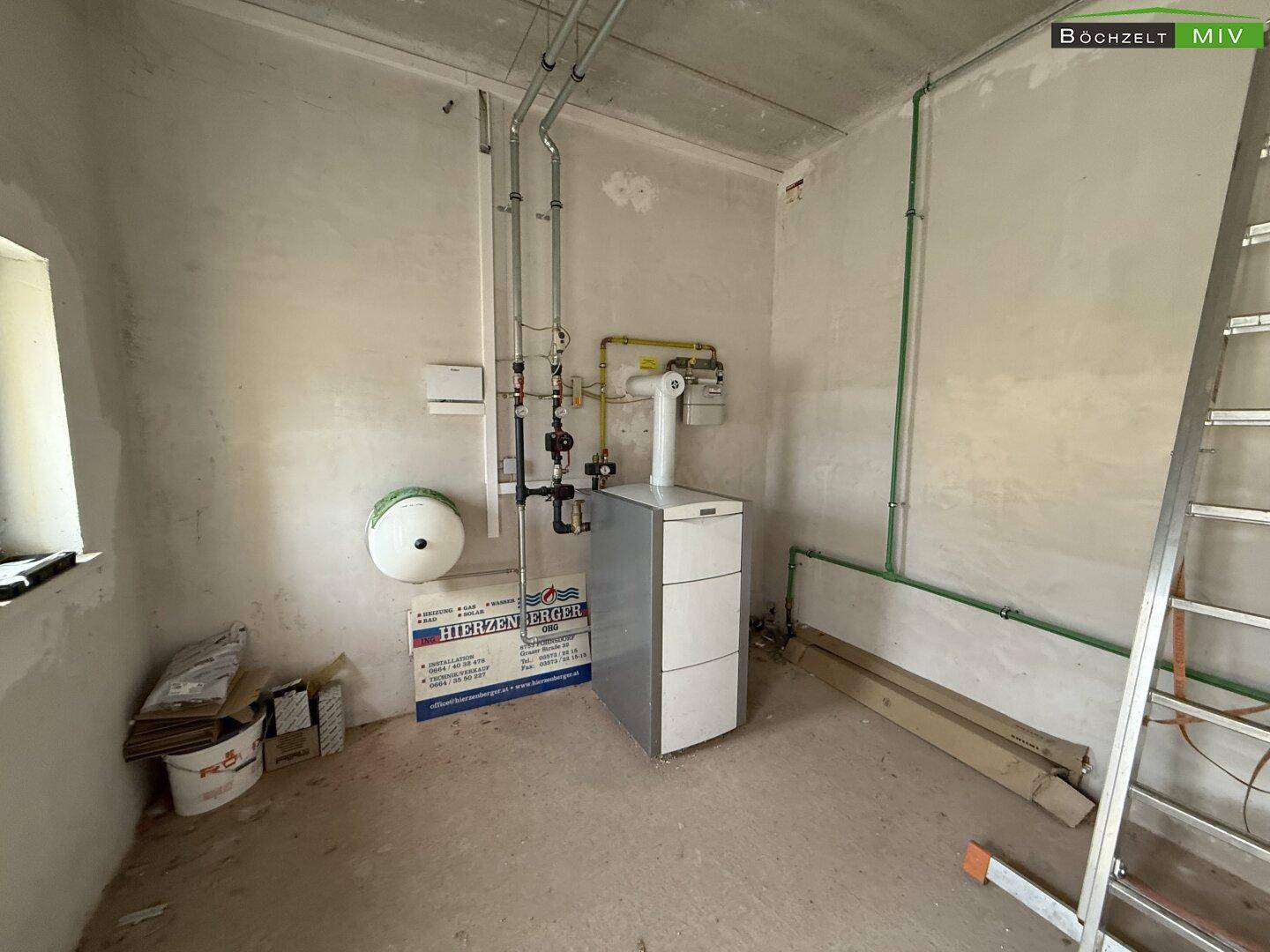 Technikraum mit Heizungsanlage, sichtbaren Rohren und einem kleinen Fenster, in einem funktionalen Zustand.