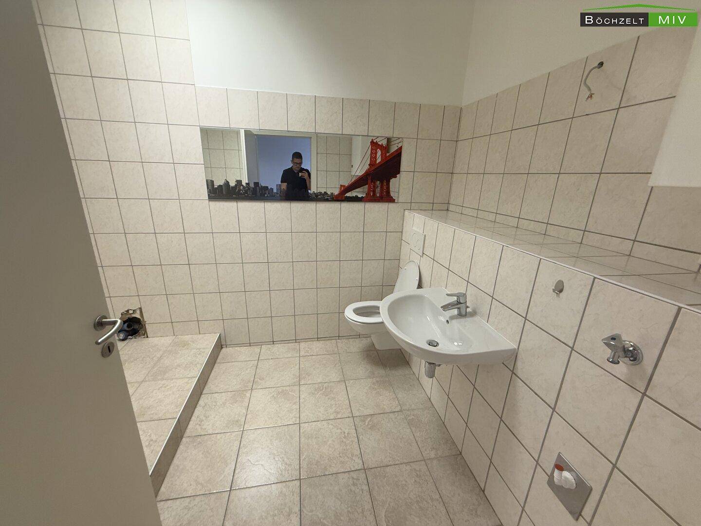 Gefliestes Badezimmer mit Waschbecken, Toilette und einem großen Spiegel, der den Raum optisch erweitert.