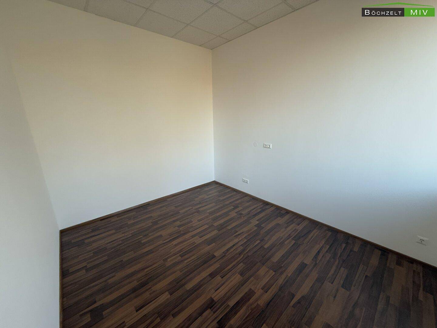 Leerer Büroraum mit dunklem Laminatboden und weißen Wänden, ideal für verschiedene Nutzungskonzepte.