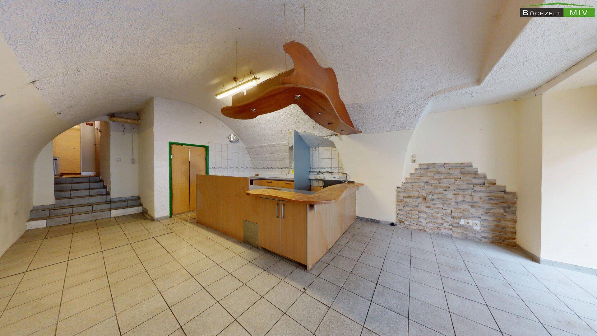 Geräumiger Gewerberaum mit gefliestem Boden, gewölbter Decke und einer Theke mit Steinwandakzent.