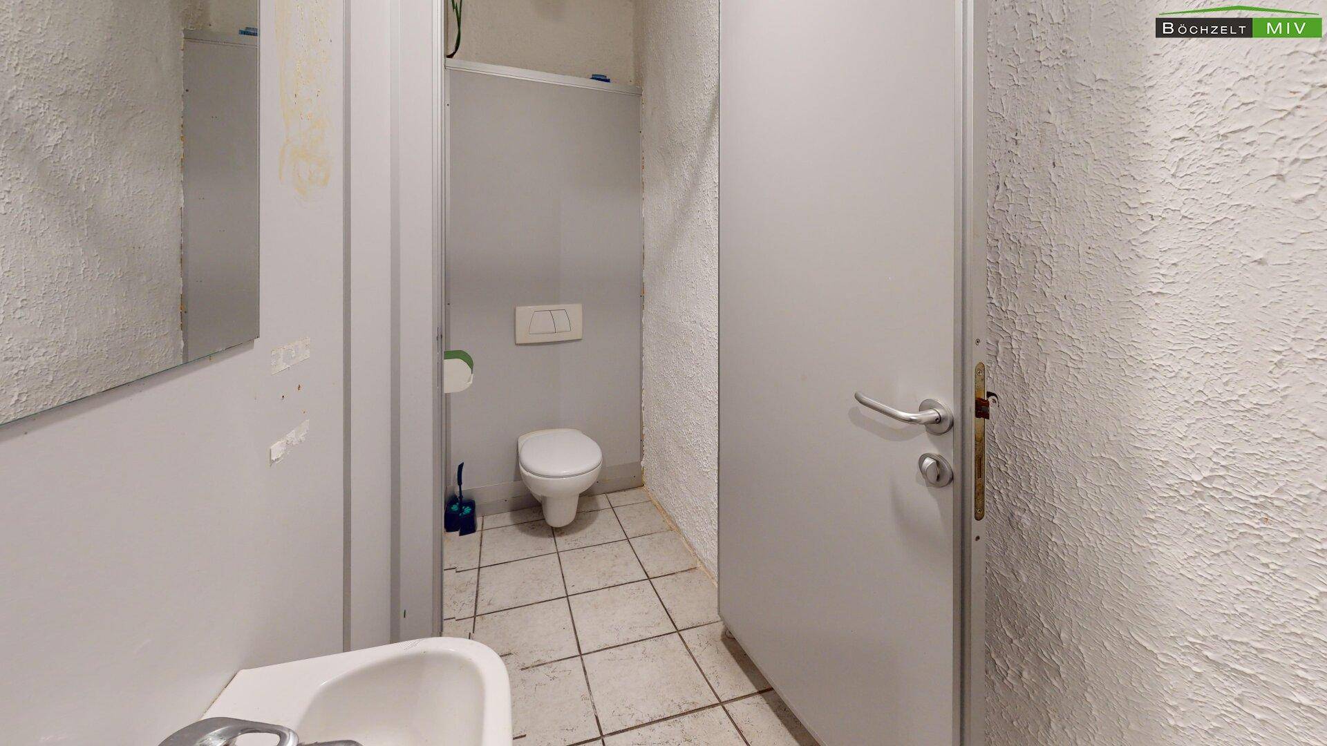Toilettenraum mit WC, Waschbecken und gefliestem Boden, in einfachem, funktionalem Zustand.