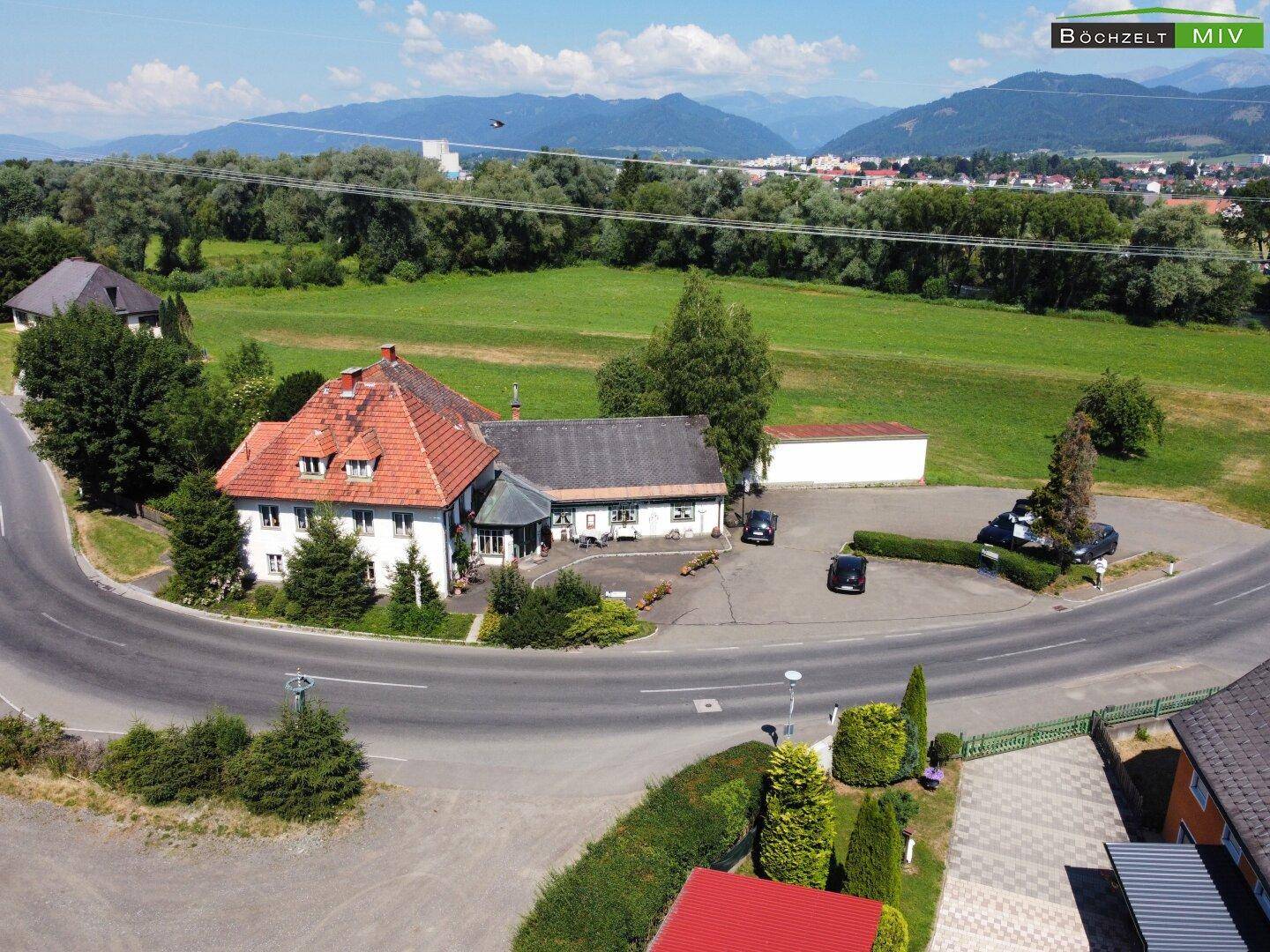Weitläufige Luftaufnahme des Anwesens mit umliegenden Feldern, einer Straße und einer Stadt in der Ferne.