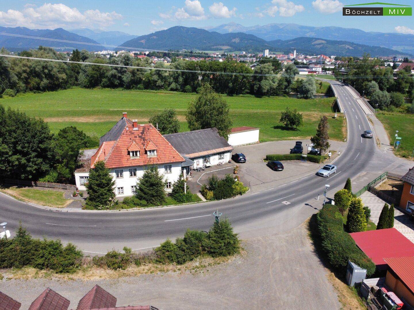 Panoramablick aus der Luft auf das Anwesen, umgeben von Natur, mit einer Brücke und Bergen im Hintergrund.