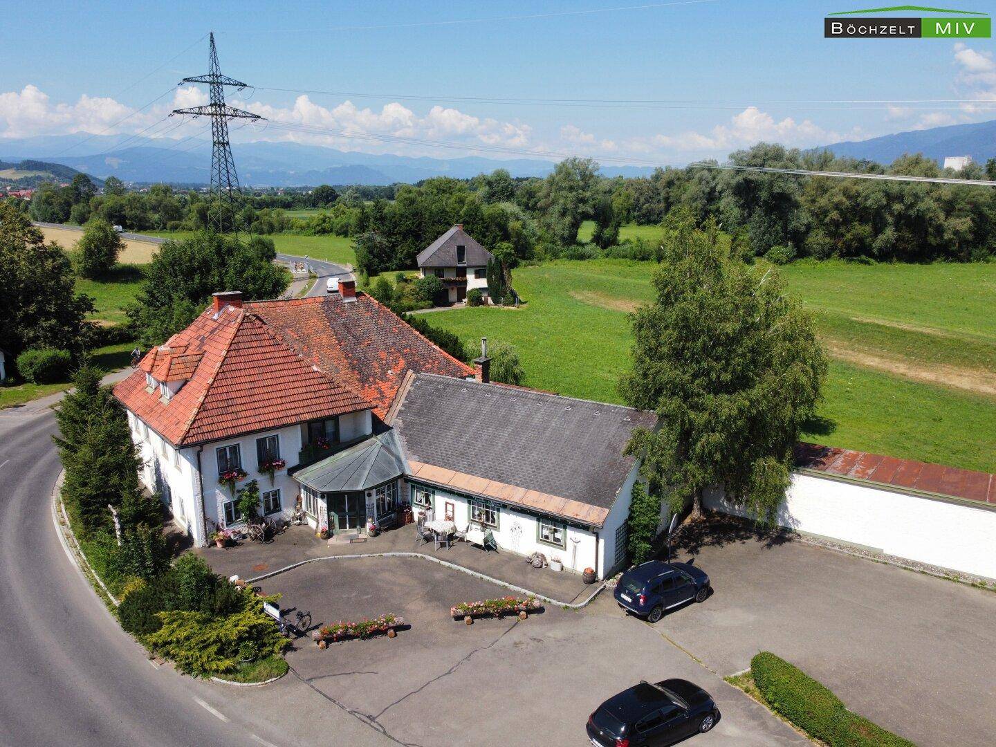 Luftaufnahme des Anwesens mit traditioneller Architektur, umgeben von Bäumen und einem großen Parkplatz.
