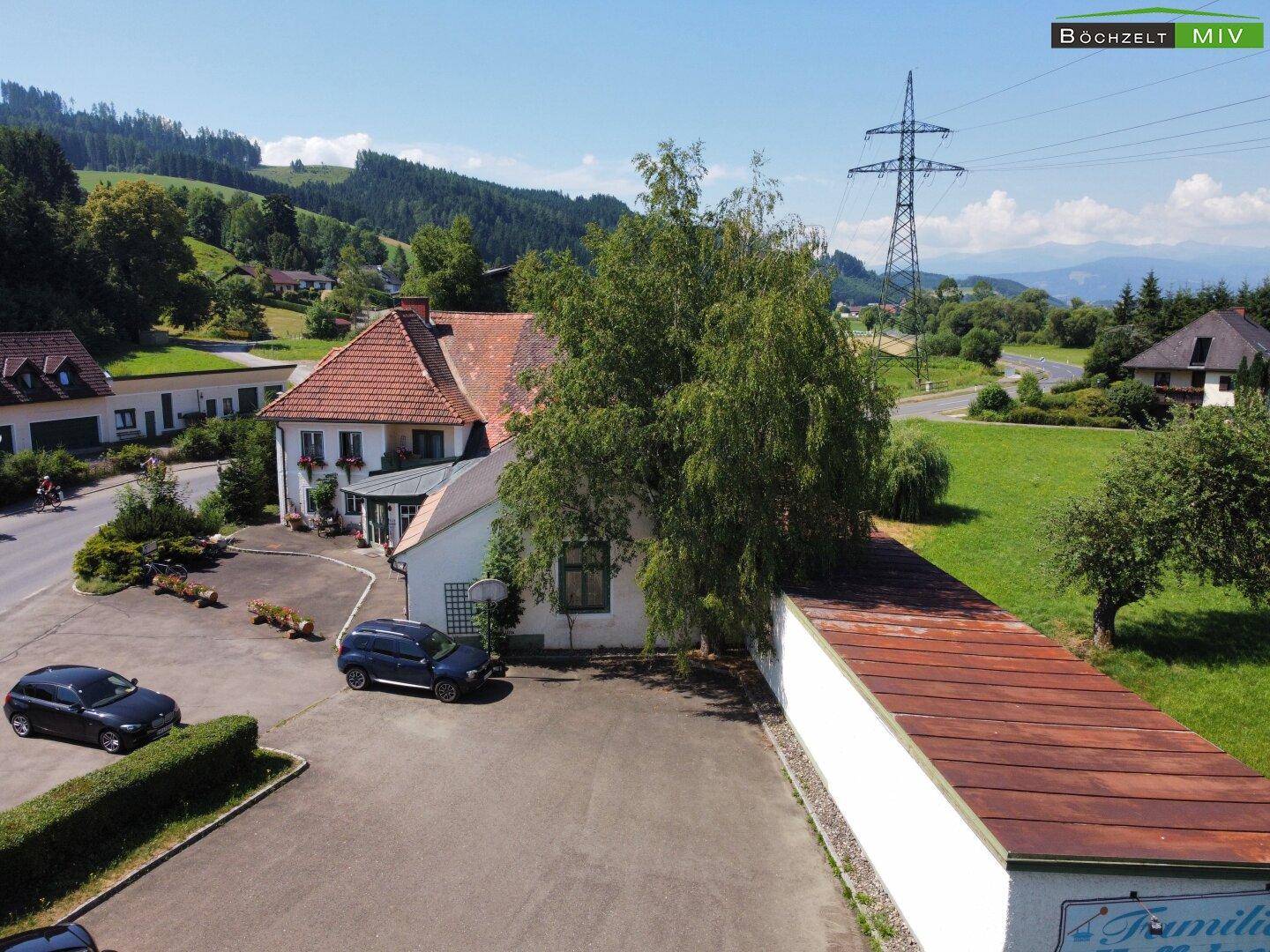 Luftaufnahme des Anwesens von der Seite, mit einem langen Anbau und hügeliger Landschaft im Hintergrund.