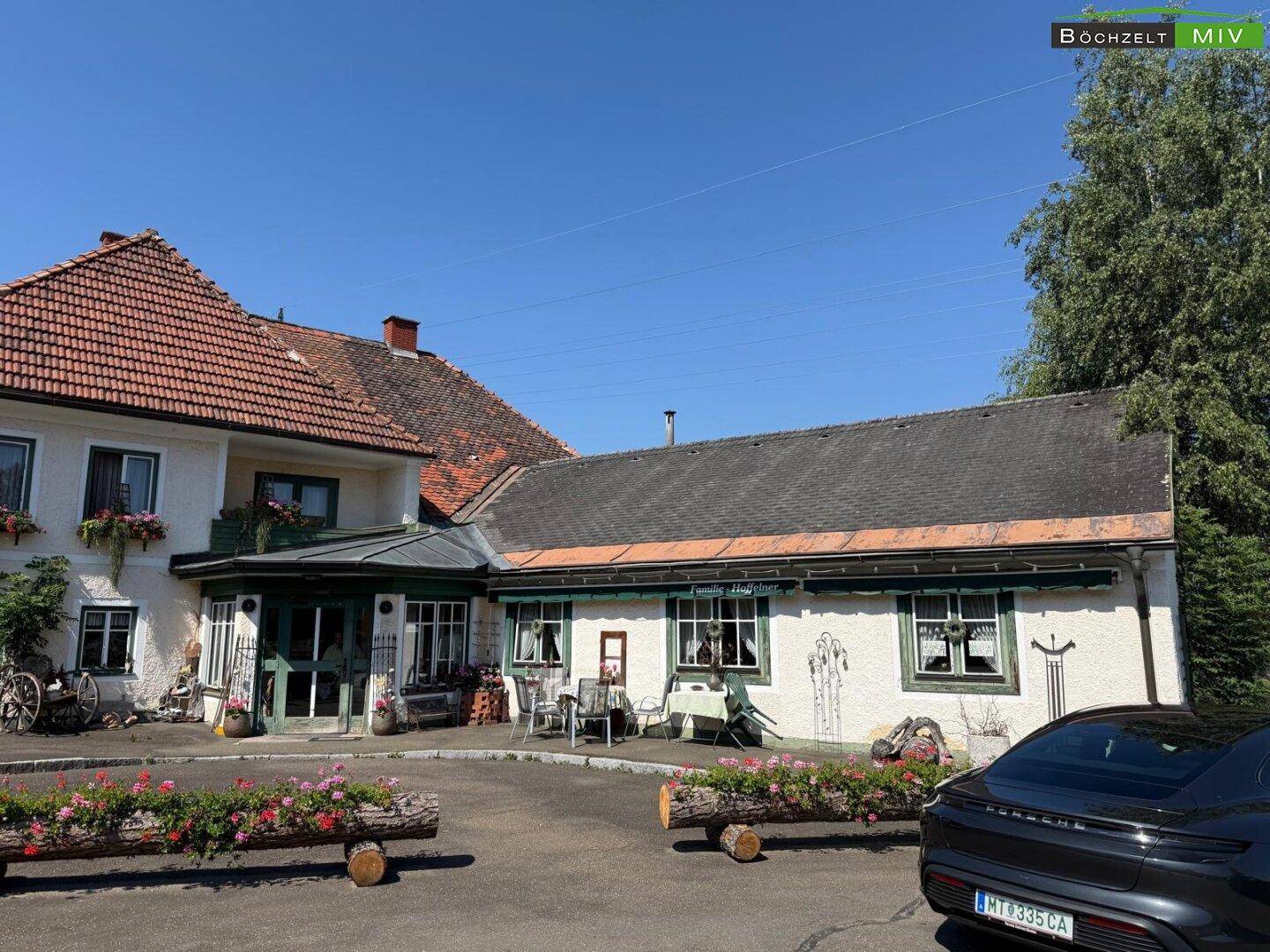 Vorderansicht des Gebäudes mit Außenterrasse, Sitzgelegenheiten und Blumenkästen aus Holzstämmen.