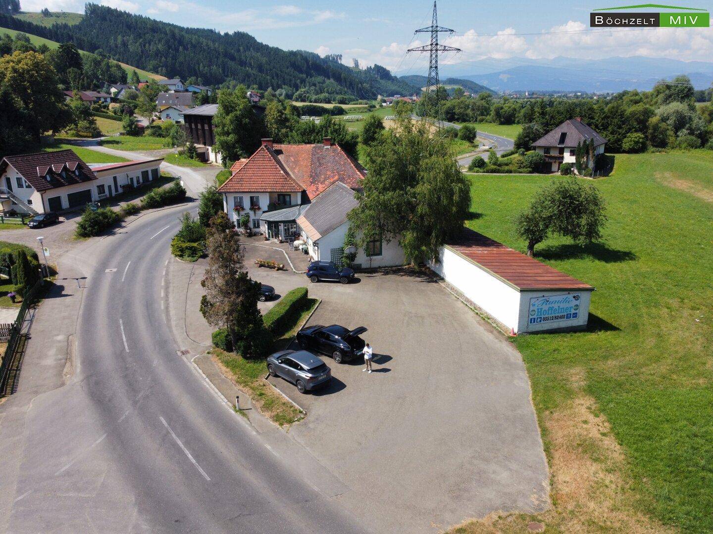 Weitwinkel-Luftaufnahme des Anwesens mit Parkplätzen, einem Nebengebäude und der bergigen Umgebung.
