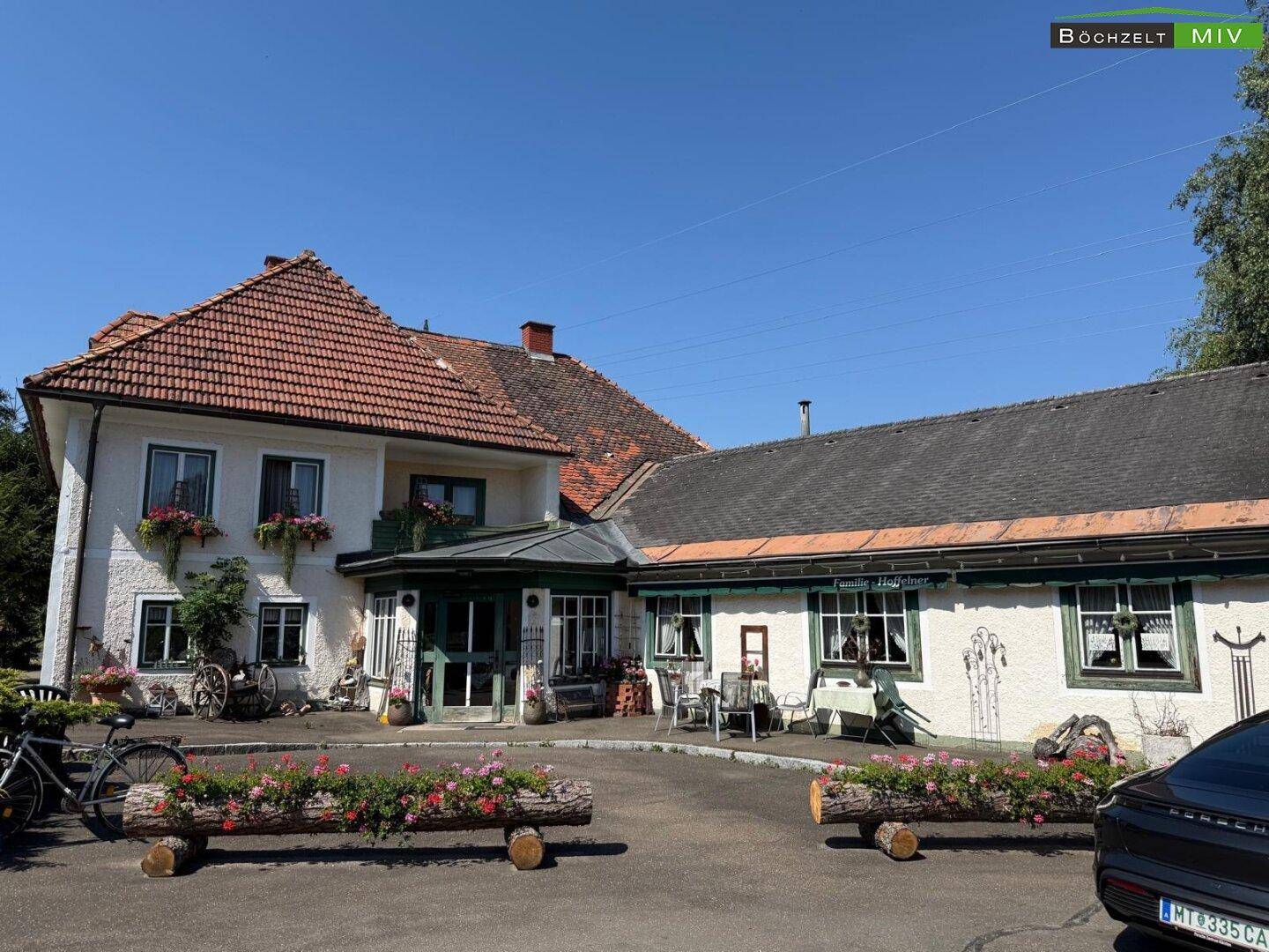 Ansicht der Gebäudevorderseite mit einladender Terrasse, Sitzgelegenheiten und traditionellen Fensterläden.