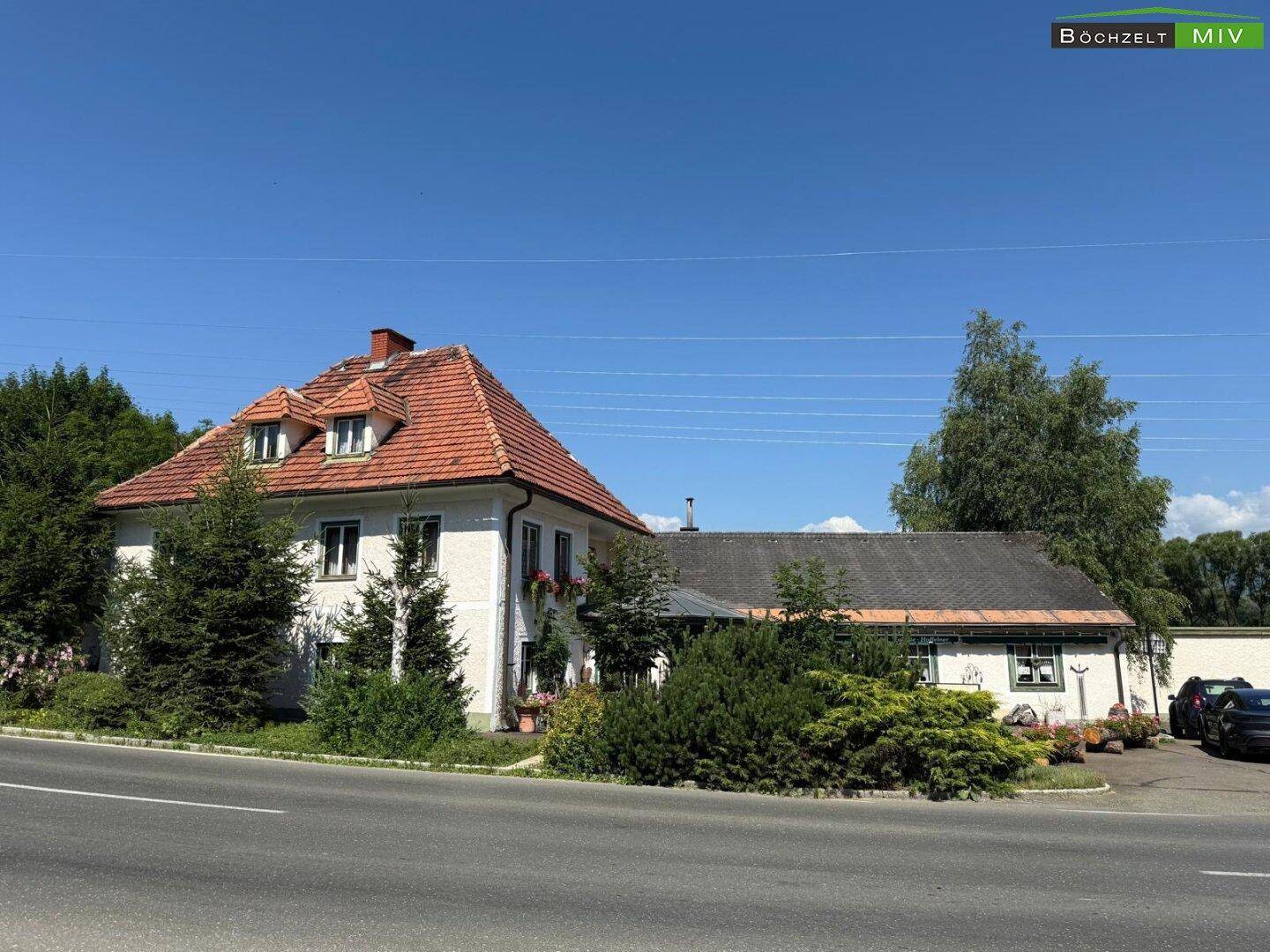 Ansicht des traditionellen Gebäudes von der Straße aus, mit rotem Ziegeldach und grüner Bepflanzung.