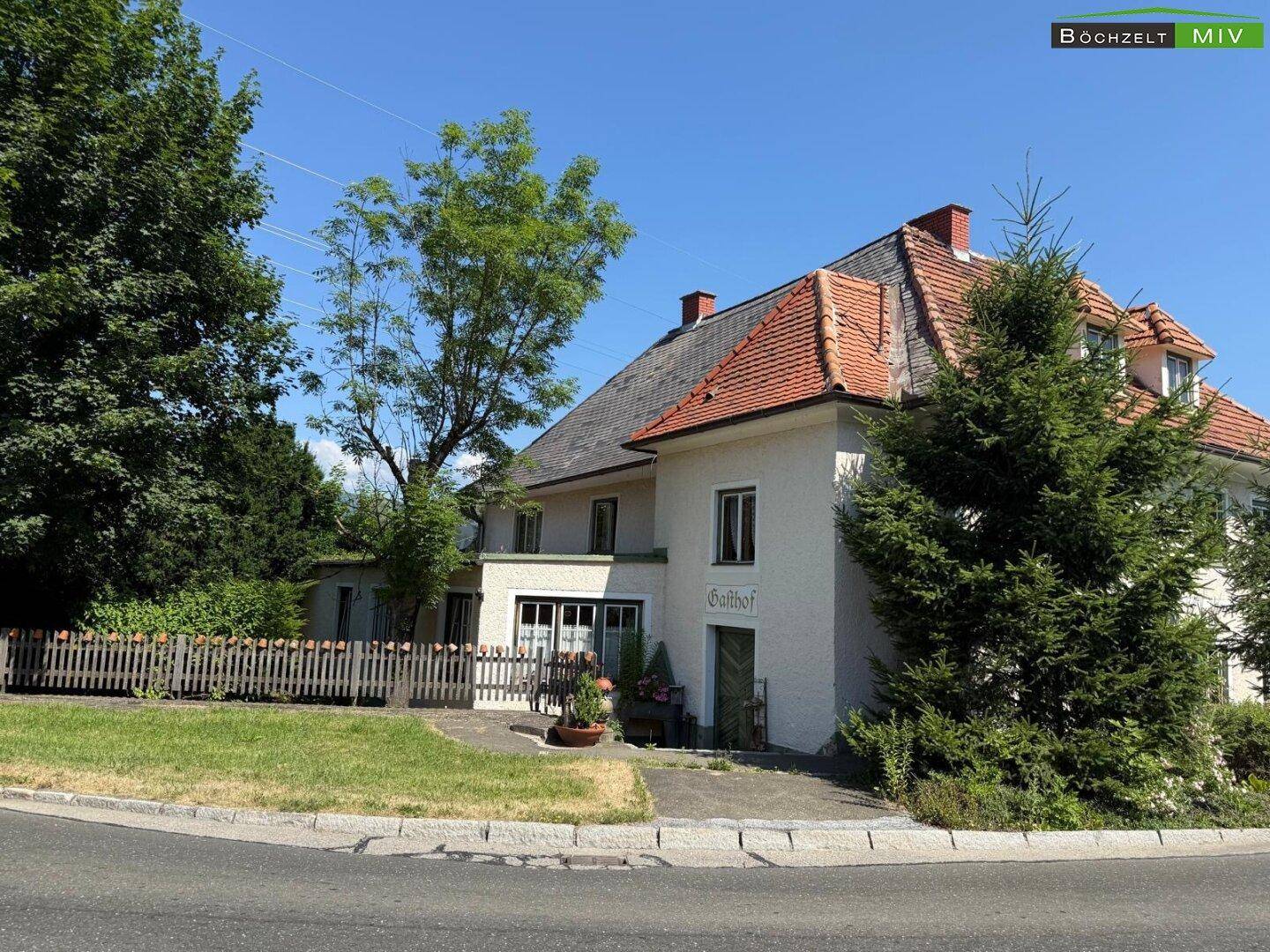 Traditionelles Gasthofgebäude mit weißer Fassade und rotem Ziegeldach, umgeben von Bäumen und Grünflächen.