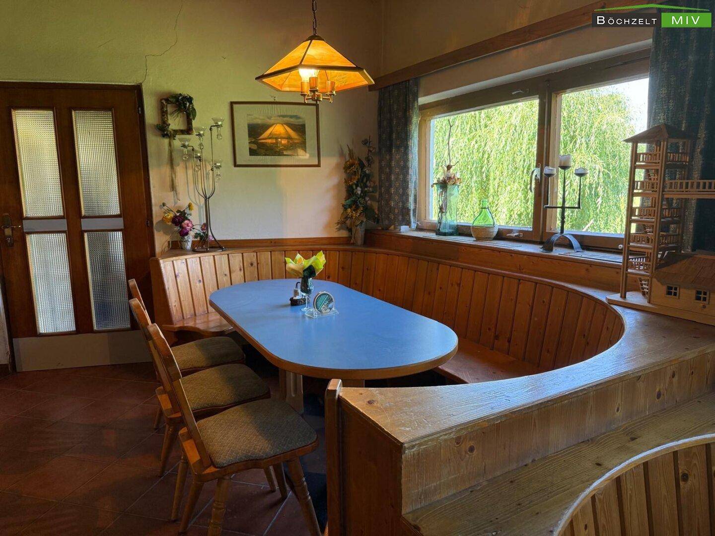 Gemütlicher Essbereich mit rustikaler Holzeinrichtung, Eckbank und Blick ins Grüne durch ein großes Fenster.