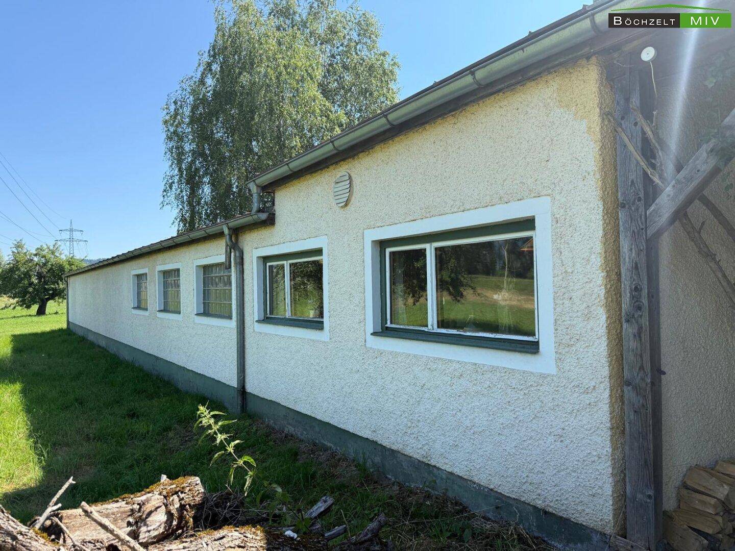 Lange Seitenfassade des Gebäudes mit mehreren Fenstern und einfacher Putzstruktur, umgeben von Gras.