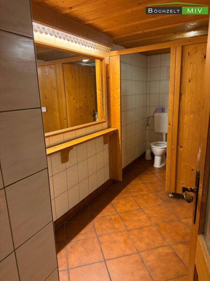 Rustikale Toilettenanlage mit Holzverkleidung, Fliesenboden und einem großen Spiegel über dem Waschbeckenbereich.