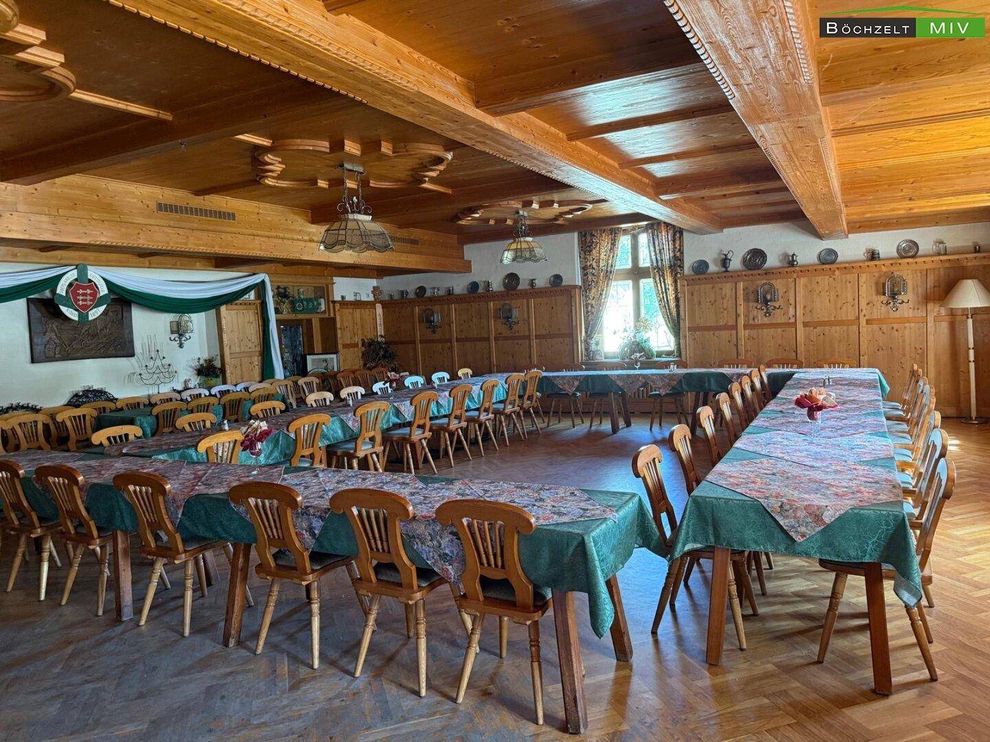 Großer Festsaal mit Holzbalkendecke, vielen Tischen und Stühlen, bereit für eine Veranstaltung.