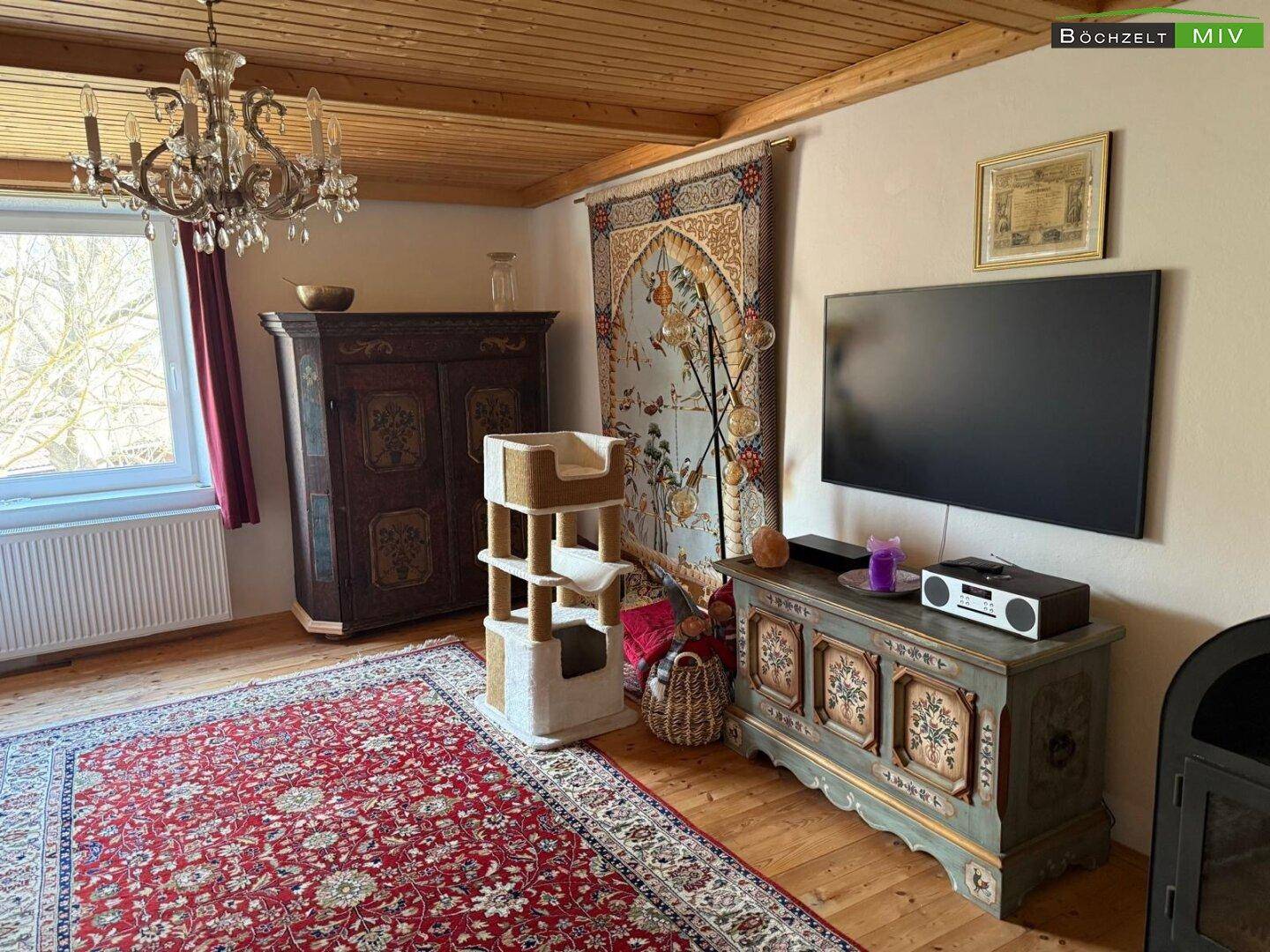 Gemütliches Wohnzimmer mit Holzbalkendecke, Teppichboden und traditionellen Möbeln.