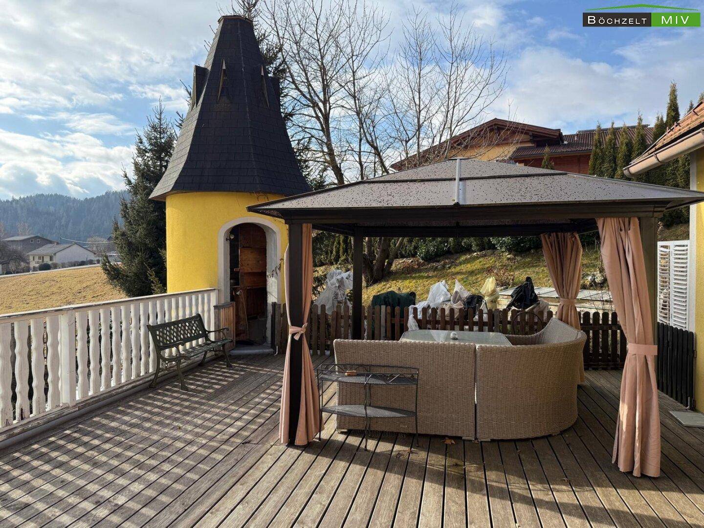 Große Holzterrasse mit gemütlicher Lounge-Sitzgruppe und Blick auf die umliegende Landschaft.