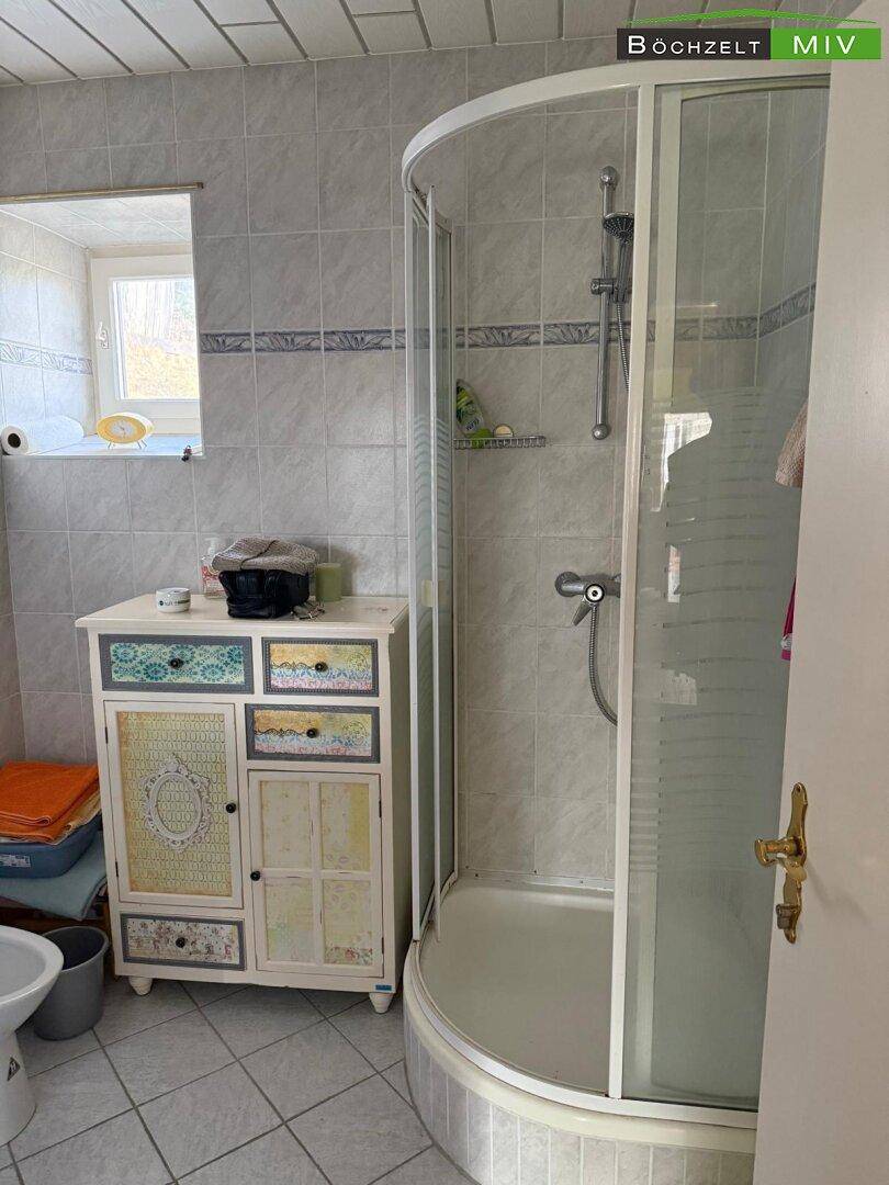 Badezimmer mit Duschkabine, Fenster und einem farbenfrohen Waschtischunterschrank.