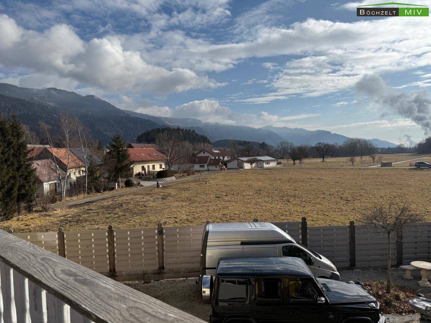 Weitläufiger Blick auf die umliegende Berglandschaft und Felder unter bewölktem Himmel.